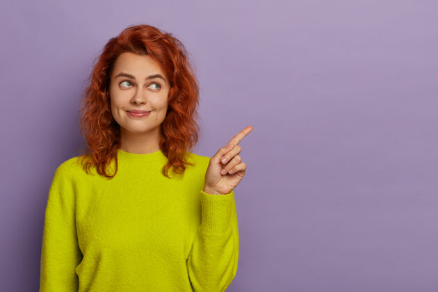 欢呼红发美女将食指指向一边 身着亮黄色套头衫 展示广告内容或促销的复制空间 建议使用空白处获取信息紫色红色内