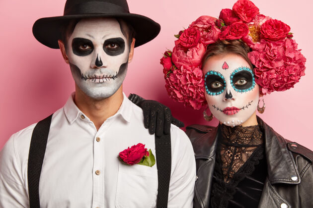 家伙严肃的女人和男人有传统的墨西哥形象 戴着糖头骨 穿着化装舞会的特殊服装 站得很近 孤立在粉色背景下狂欢节幽灵两个