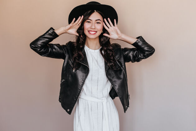 梦幻一个戴着黑帽子的兴奋的中国女人看着镜头一个穿着皮夹克的亚洲模特微笑着摆姿势黑发微笑享受