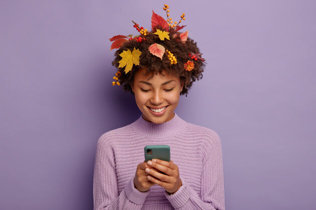 紫色快乐的卷发女人通过手机和朋友聊天 有温柔的微笑 头上有黄色的叶子美国非洲使用