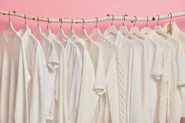 服装白色纯色衣服一排挂在木制衣架上 粉色背景是零售店女性的大选择粉色时尚精品