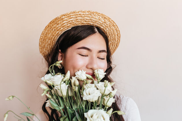 亚洲戴草帽的亚洲妇女闭着眼睛闻花香的肖像摄影棚拍摄的手持一束白色桔梗的日本美女草帽表情情感