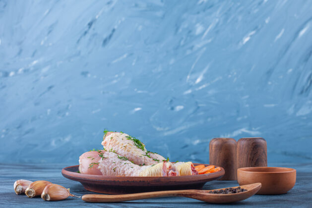 木盘把腌好的鸡腿和切成片的胡萝卜放在木盘上 旁边放着香料 勺子和大蒜 放在蓝色的表面上开胃菜菜肴蔬菜