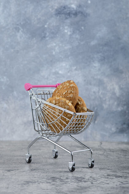 谷物石头桌上放着一辆粉红色的小推车 里面放着健康的燕麦片饼干饼干芝麻脆