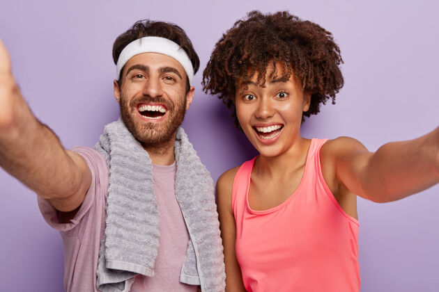 表情运动型情侣在健身后自拍 面带笑容 表达良好的情绪 穿着休闲服 双手伸直 过着健康的生活方式 隔着紫色的墙锻炼 训练运动两个欢呼