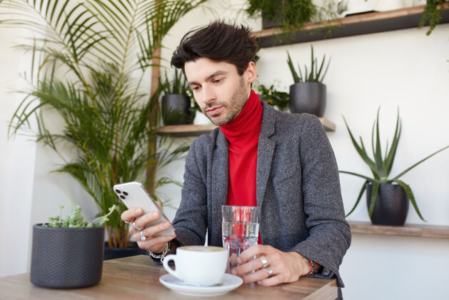 优雅年轻迷人的棕色头发的男人坐在城市咖啡馆夹克男性手机