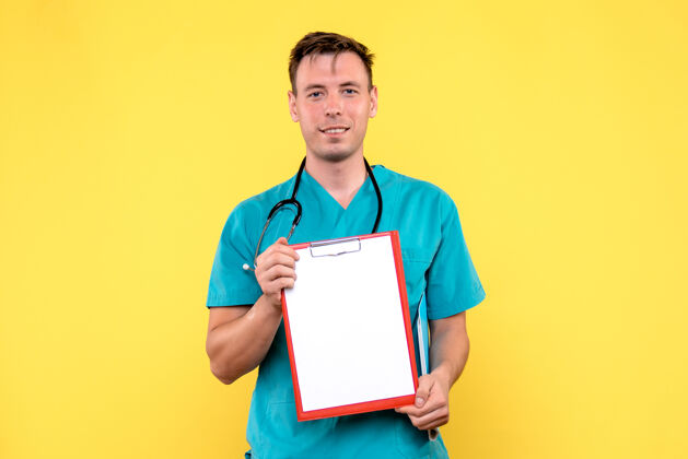 医疗年轻的男医生在黄色的墙上拿着分析的正面图人笔记本抱