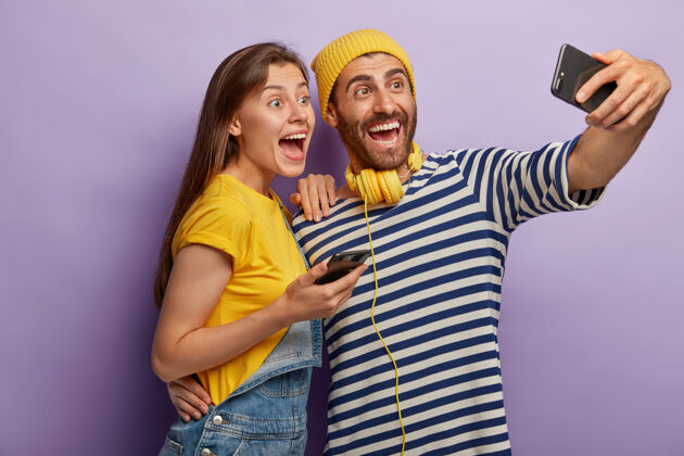 自拍两个有趣的男女朋友在智能手机上自拍 在娱乐时间玩得开心 使用现代手机应用程序耳机情侣女孩