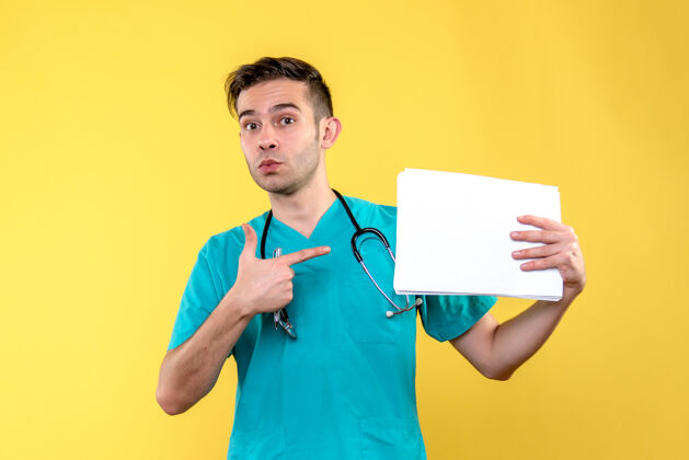 人黄色墙上挂着文件的年轻男医生的正视图护士医学微笑