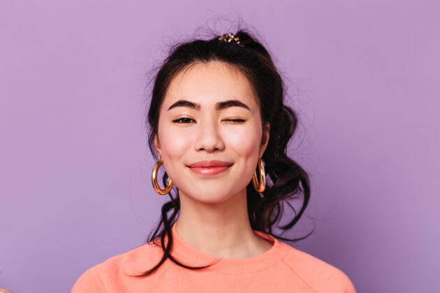 卷发戴着耳环微笑的亚洲女人的正视图紫色背景上孤立的快乐中国女人的摄影棚镜头漂亮肖像模特