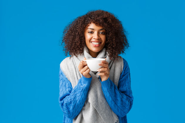时尚迷人的笑容可掬的美籍非洲裔快乐女人 卷发 裹着围巾 喝着咖啡 蓝色的墙壁茶房子立场