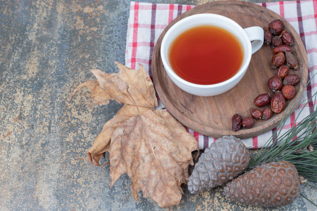 干的一杯红茶和干玫瑰果放在松果木盘上高质量的照片草饮料桌布