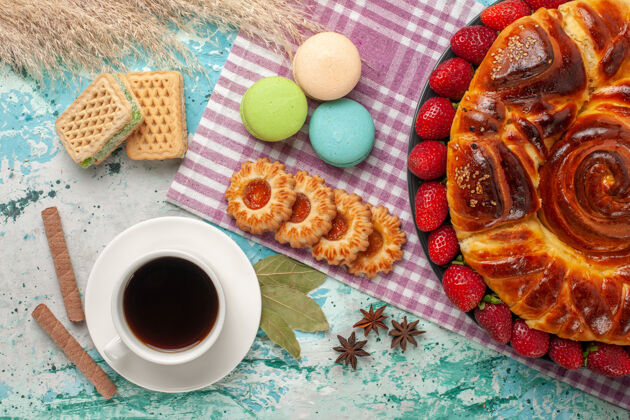食物俯瞰草莓派与茶杯饼干和法国马卡龙在蓝色的表面早餐桌子蛋糕