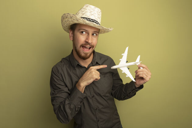男人穿着灰色衬衫 戴着夏帽的年轻帅哥拿着玩具飞机 用食指指着它快乐而积极帅气衬衫目录