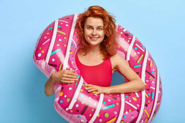 人美丽的千禧一代女人 红色卷发 在蓝色的墙上摆着一副油炸圈饼的姿势快乐年轻娱乐