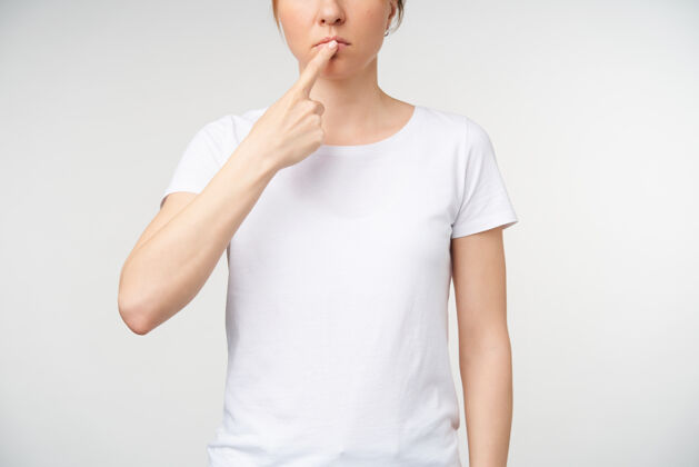 成人自然妆容的年轻女士保持食指放在嘴唇上 同时在手语上展示工作舌头的不规则镜头 站在白色背景上特写语言符号