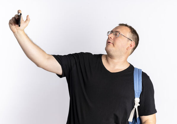 男人一个戴眼镜 身穿黑色t恤的超重男子站在白墙上用智能手机自拍站立自拍超重