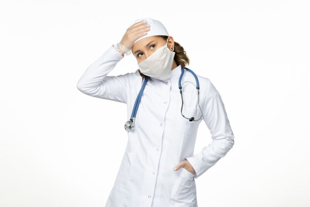 病毒正面图年轻女医生戴着无菌口罩和手套 由于冠状病毒在浅白的表面大流行浅白色正面