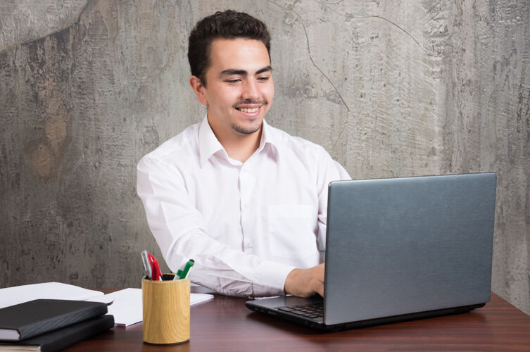 笔记本电脑微笑的商人看着笔记本电脑 坐在办公桌旁高品质的照片桌子男男