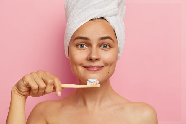 裸体笑容可掬 皮肤清新的乐观女性近照 用牙膏握牙刷 头戴白毛巾 直视 有口腔卫生程序牙科口腔医学