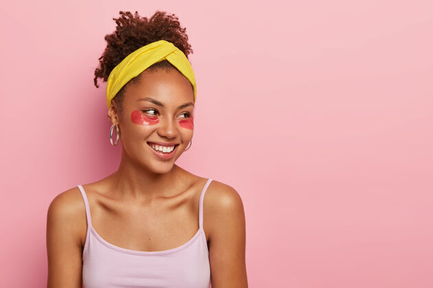 非洲人皮肤护理概念年轻的美国黑人女性 眼睛下面有胶原蛋白垫 想要拥有干净新鲜的皮肤 戴着黄色的头带和休闲背心女人自然牙齿