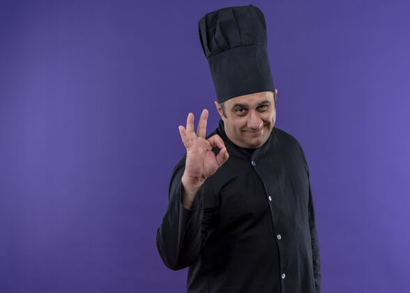 穿男厨师身穿黑色制服 头戴厨师帽 面带微笑地看着摄像机 紫色背景上立着ok标志秀紫制服