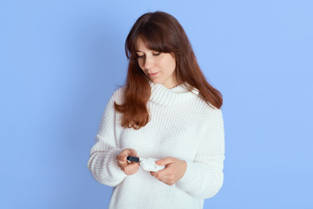 时尚沉思的年轻女子穿着白色休闲针织毛衣用烟支取暖 望着上面的蓝色 女士拿着电子烟女性热吸烟
