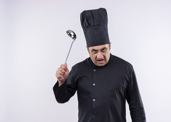 拿着男厨师身穿黑色制服 头戴厨师帽 手拿勺子 站在白色背景上怒气冲冲地看着镜头帽子站着看
