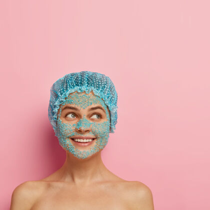积极人 纯洁和面部护理理念满意微笑的年轻女子应用蓝色海盐磨砂膏 拥有赤裸的身体 清洁焕发的皮肤 戴上淋浴帽 往旁边看 有美容程序垂直健康放松