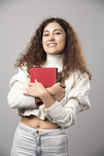 年轻年轻的微笑的女人拿着一本红色的书在灰色的墙上高质量的照片微笑女士人
