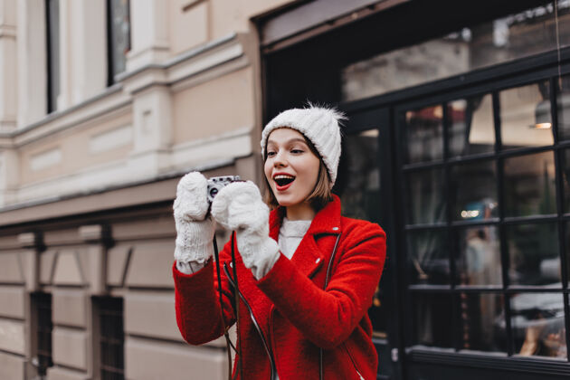 衣服穿着红色夹克 戴着针织帽子和手套的快乐女孩用复古相机为城市拍照街道温暖寒冷