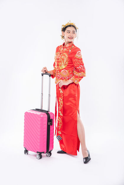 微笑女人穿旗袍套装 头戴皇冠 准备在中国新年带着粉色旅行包旅行传统服装节日旗袍
