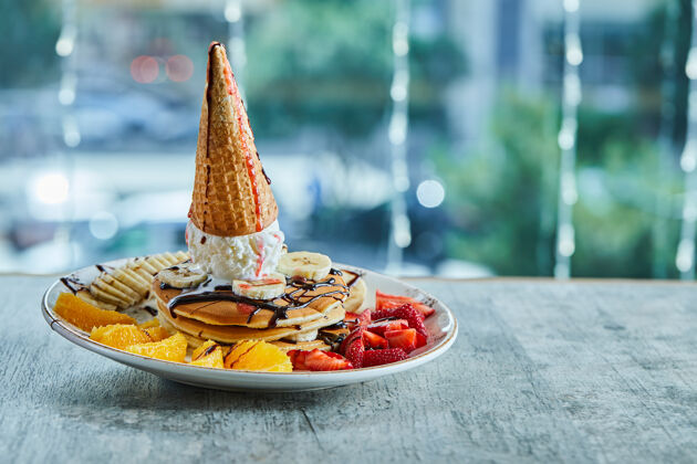 香草在大理石表面的白色盘子里放上薄饼 里面有冰淇淋筒 橘子 草莓 香蕉和巧克力糖浆草莓橘子美味