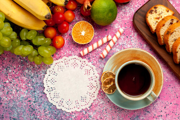 饼干俯瞰美味的水果组成与切片蛋糕和茶杯在淡粉色的办公桌上甜食成分柑橘
