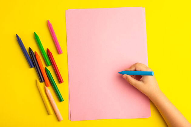 五颜六色俯视图：小孩用彩色铅笔在黄色的粉色纸上画教育使用蜡笔