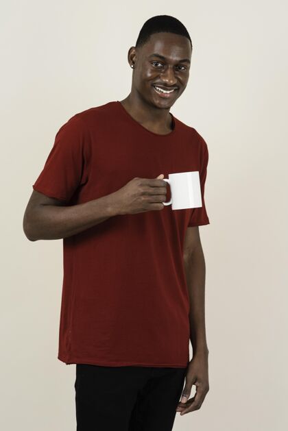 年轻笑脸人的肖像在一个t恤拿着马克杯垂直男人成人