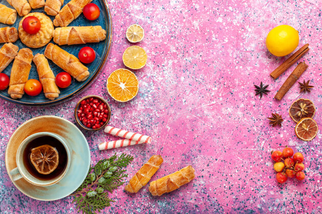 鲜花顶视图甜美美味的百吉饼在托盘内与李子和一杯茶在淡粉色的桌子上食物美味浅粉色