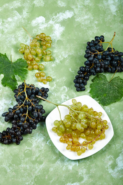 盘子一盘白葡萄和黑葡萄 绿色表面有叶子一串甜美多汁
