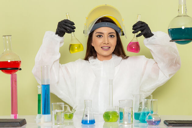 医生正面图身着特殊防护服的年轻女性化学家在绿色办公桌上工作化学工作女性科学实验室溶液科学防护