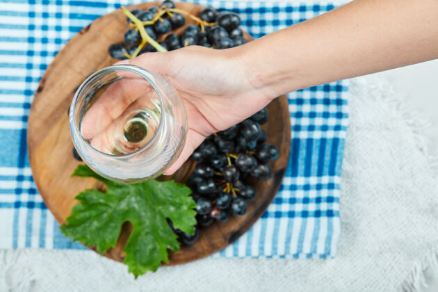 葡萄一束黑葡萄放在带叶子的木盘上 手里拿着一只空杯子特写桌布集群