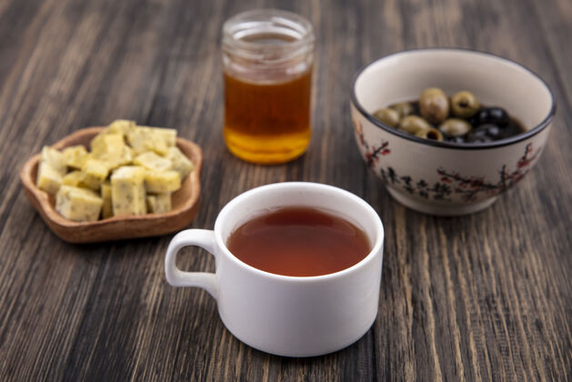 蜂蜜一杯蜂蜜 橄榄和切碎的奶酪片放在木制背景上的茶的俯视图茶杯子景观