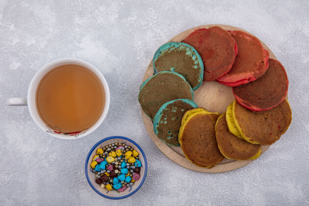 杯子俯瞰彩色煎饼架上的彩色巧克力和一杯茶的白色背景薄煎饼支架茶