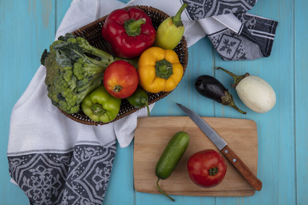 刀用刀在砧板上切黄瓜西红柿和甜椒 篮子里放西兰花 蓝绿色背景上放茄子西兰花篮子食物
