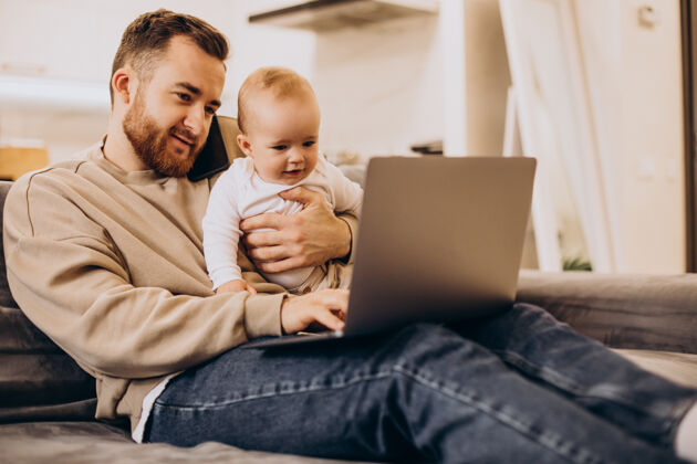 在线年轻的父亲和他的女婴坐在一起 在家里用电脑教育快乐女儿
