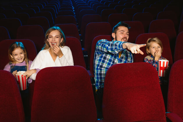 表达年轻的白种人家庭在电影院 房子或电影院看电影看起来富有表现力 惊讶和情绪化独自坐着玩关系 爱情 家庭 童年 周末时间约会看情绪