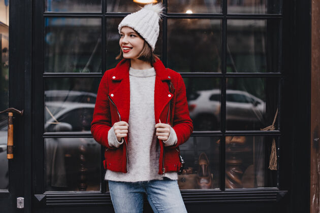 地图时尚的女士心情很好 靠在黑色木框的窗户上女孩穿着牛仔裤 帽子和红色夹克摆姿势毛衣长相针织