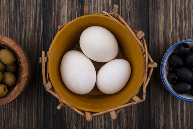 营养顶视图鸡蛋在一个篮子里 黑色和绿色的橄榄在木制背景的碗里木头碗景观