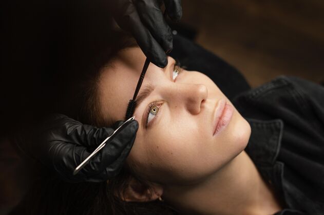 专家高角度的女临床医生为女顾客做美眉治疗镊子手术美容