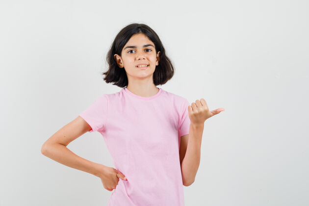 自信穿着粉色t恤的小女孩用拇指指着旁边 看上去很自信 正对着前方漂亮时尚青少年