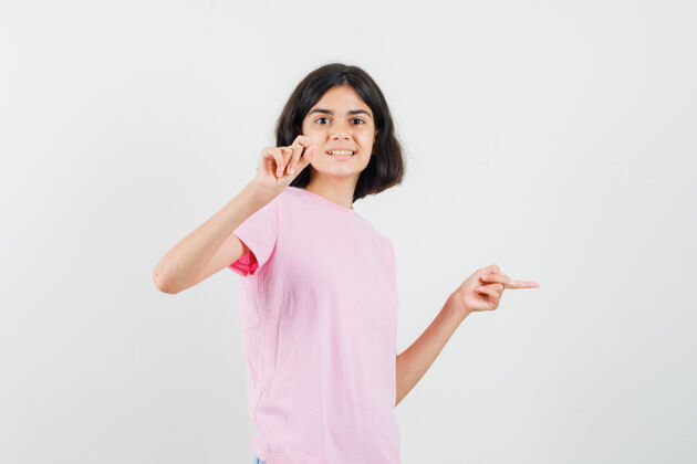 可爱小女孩指着旁边 展示着小尺寸的标志 穿着粉色t恤 看上去很欢快 正前方视图和平青少年外观